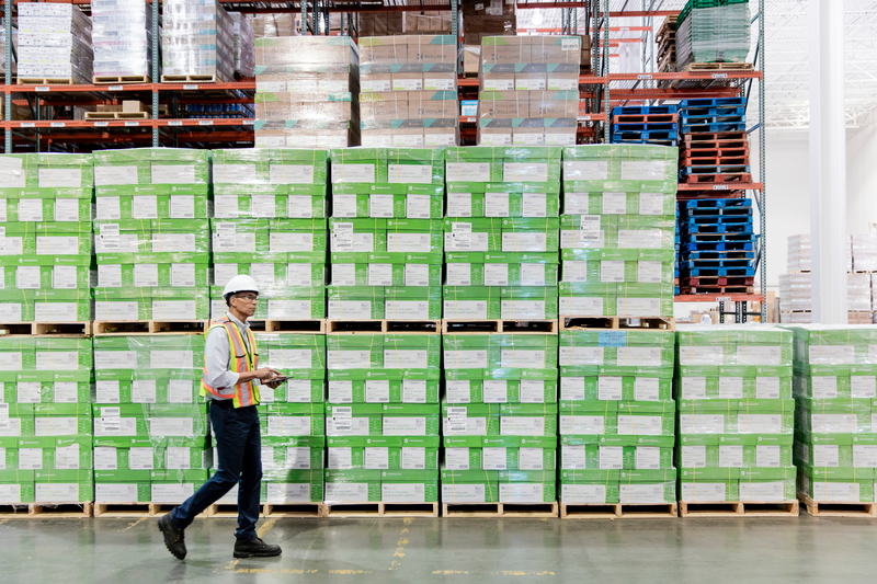 Side view of man walking by stacked pallets for shipping in industrial warehouse. 300% ENLARGEMENT AVAILABLE FOR EVENT USE.